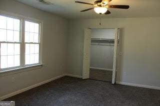 unfurnished bedroom featuring dark colored carpet, a closet, a ceiling fan, and baseboards