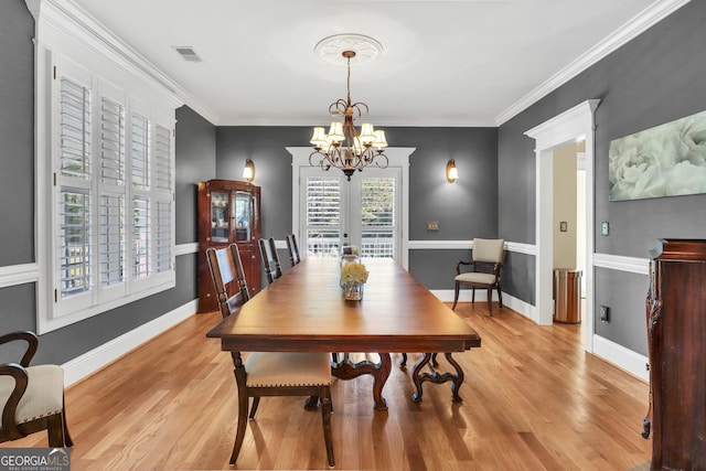 dining room with an inviting chandelier, ornamental molding, light wood-type flooring, and french doors