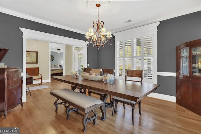 dining space with an inviting chandelier, ornamental molding, and light hardwood / wood-style floors