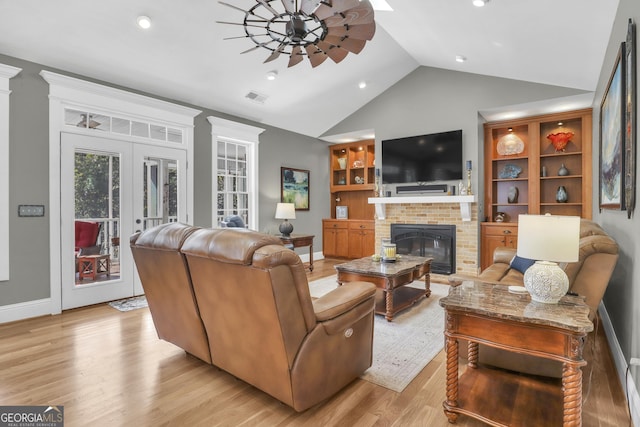 living room with a fireplace, ceiling fan, vaulted ceiling, light hardwood / wood-style floors, and french doors