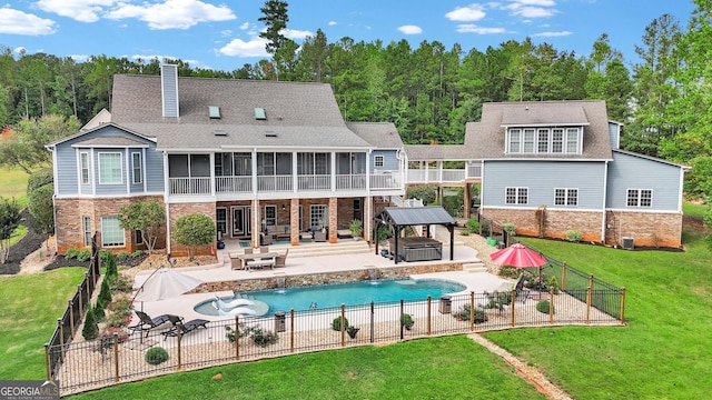 rear view of house with pool water feature, a sunroom, a patio, a lawn, and a swimming pool with hot tub