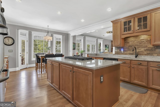 kitchen with black gas stovetop, a kitchen island, light stone counters, sink, and tasteful backsplash