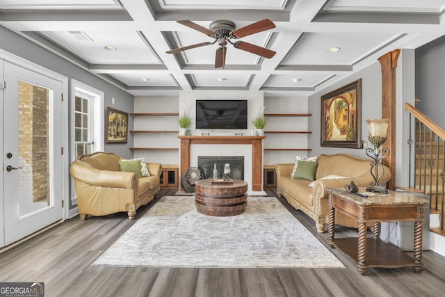 sitting room featuring light hardwood / wood-style flooring, ceiling fan, beam ceiling, coffered ceiling, and a brick fireplace