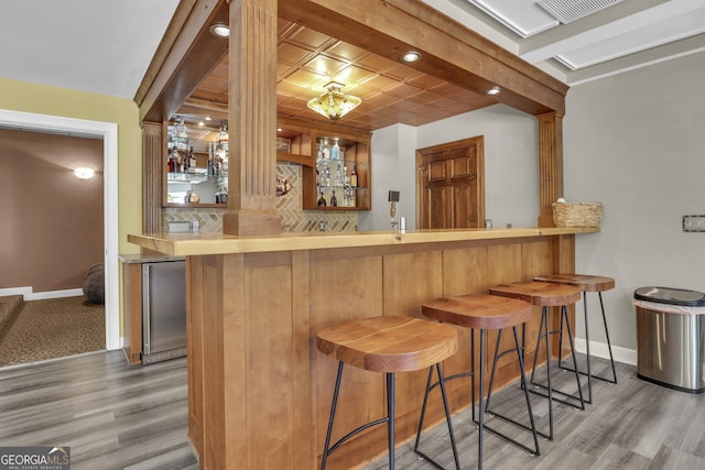 bar with wood finished floors, baseboards, indoor bar, and backsplash