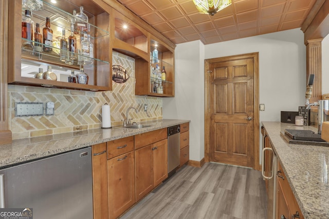 kitchen with light hardwood / wood-style flooring, backsplash, stainless steel dishwasher, sink, and light stone countertops