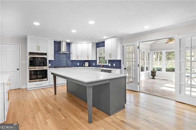 kitchen featuring stainless steel double oven, a kitchen island, wall chimney exhaust hood, white cabinets, and a kitchen breakfast bar