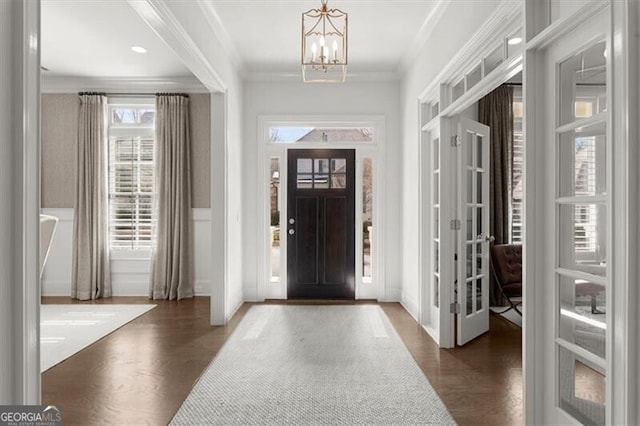 foyer entrance featuring a notable chandelier, ornamental molding, and wood finished floors