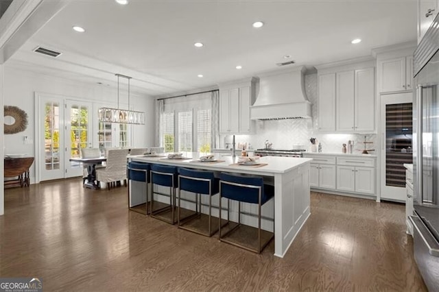 kitchen with dark wood-style flooring, light countertops, custom range hood, visible vents, and white cabinetry