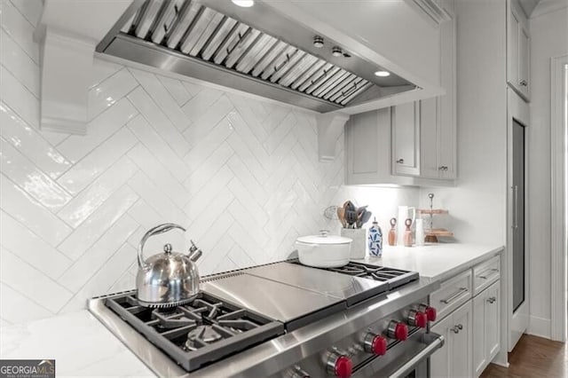 kitchen featuring light countertops, high end stove, premium range hood, and decorative backsplash