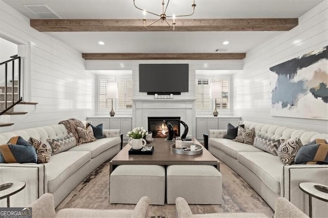 living area featuring a chandelier, a warm lit fireplace, beamed ceiling, and stairs