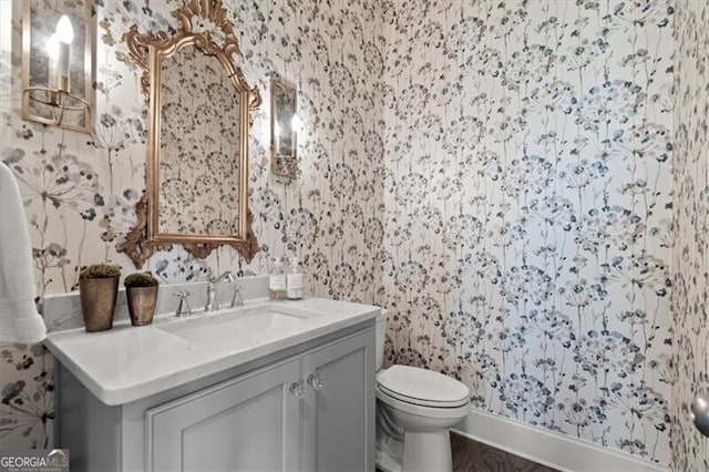 bathroom with toilet, vanity, and wallpapered walls