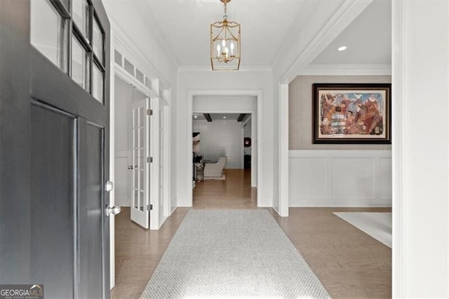 foyer entrance with crown molding, a decorative wall, wainscoting, wood finished floors, and a chandelier