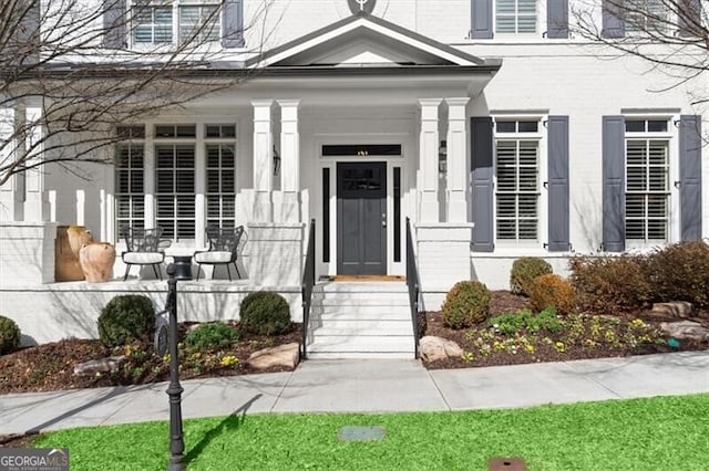 entrance to property featuring a porch and brick siding