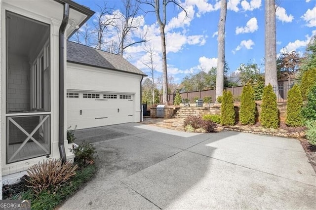 view of side of property featuring a garage, driveway, a shingled roof, and fence