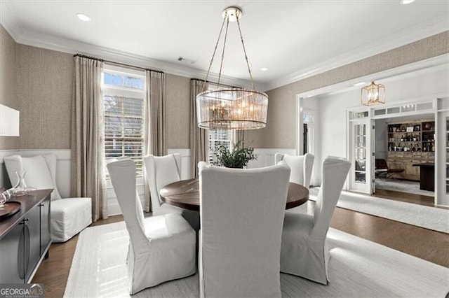 dining area featuring a chandelier, wood finished floors, visible vents, ornamental molding, and wallpapered walls