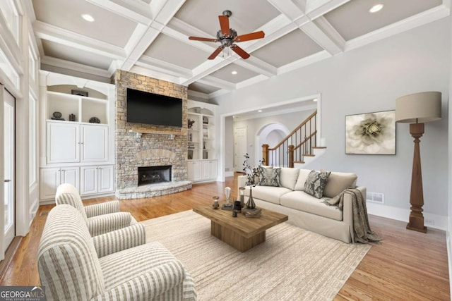 living area featuring light wood-style flooring, a fireplace, coffered ceiling, and beamed ceiling