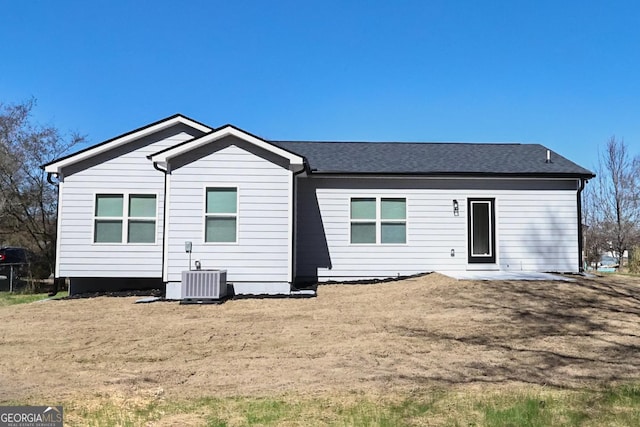 rear view of property featuring central air condition unit, a shingled roof, and a yard