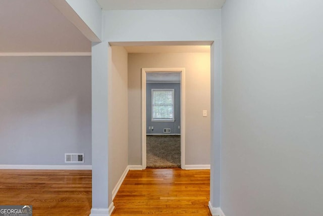 corridor with baseboards, visible vents, and wood finished floors