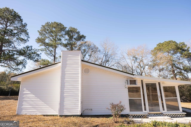 view of side of home with a sunroom and a chimney