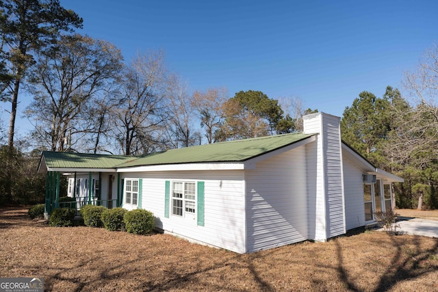 view of side of home with metal roof, a chimney, and a porch