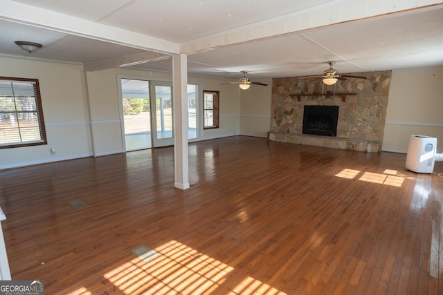 unfurnished living room featuring baseboards, a stone fireplace, a wealth of natural light, and wood finished floors