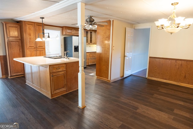 kitchen featuring light countertops, brown cabinets, decorative light fixtures, an island with sink, and wainscoting