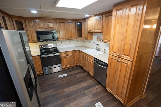 kitchen featuring a sink, light countertops, appliances with stainless steel finishes, brown cabinetry, and glass insert cabinets