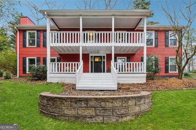 rear view of house featuring a balcony, a chimney, a porch, and a yard