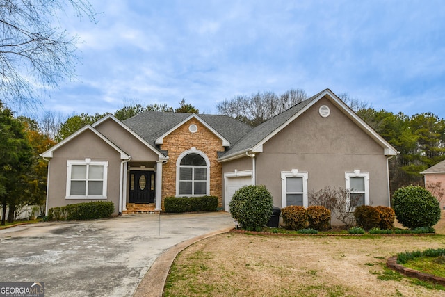 view of front of home featuring roof with shingles, stucco siding, a garage, stone siding, and a front lawn