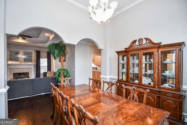 dining room with arched walkways, dark wood-style flooring, a fireplace, ornamental molding, and ceiling fan with notable chandelier