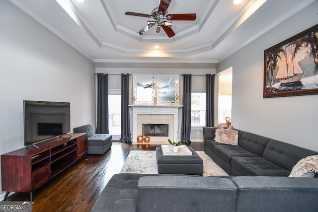 living room with ornamental molding, a tray ceiling, a tile fireplace, and dark wood finished floors