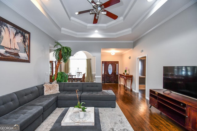 living room with ornamental molding, a tray ceiling, dark wood finished floors, and ceiling fan