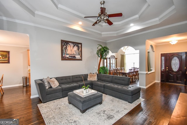 living area with arched walkways, dark wood-style flooring, a raised ceiling, ornamental molding, and baseboards