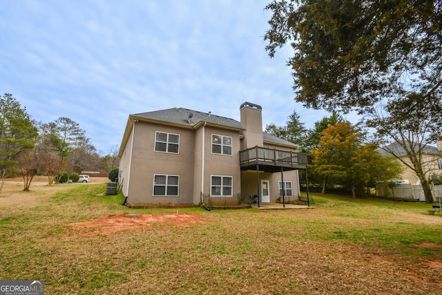 back of property with a wooden deck, a chimney, a lawn, and stucco siding