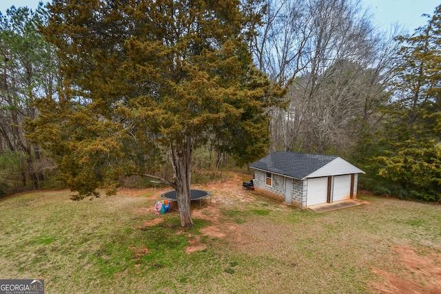 view of yard with a garage, a trampoline, and an outbuilding