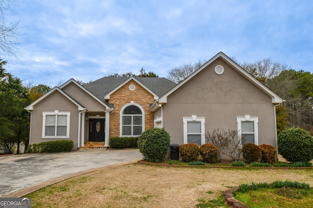 view of front of home with stone siding, a shingled roof, a front yard, and stucco siding