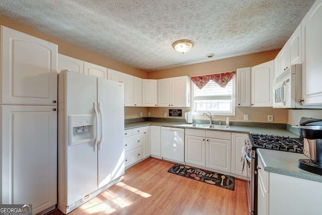 kitchen featuring white cabinets, a sink, white appliances, a textured ceiling, and light wood-type flooring