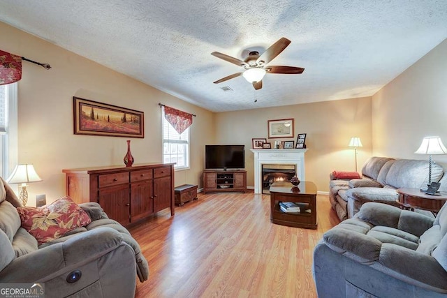 living area featuring a ceiling fan, light wood finished floors, visible vents, and a lit fireplace