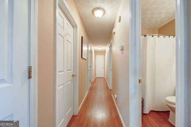 corridor with baseboards, a textured ceiling, and wood finished floors