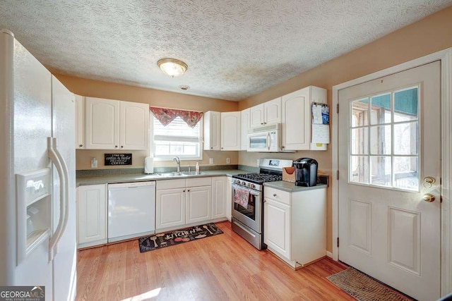 kitchen with light countertops, a sink, white cabinets, white appliances, and light wood-type flooring