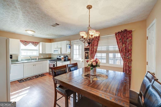 dining room featuring a textured ceiling, an inviting chandelier, visible vents, and light wood-style floors