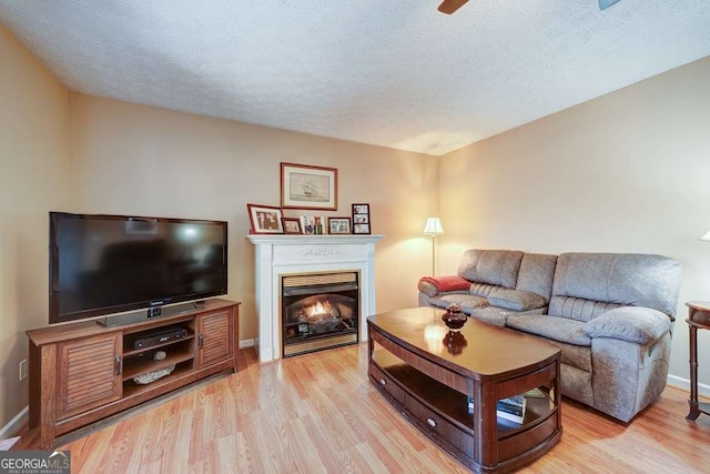 living room with a textured ceiling, a lit fireplace, and light wood-type flooring