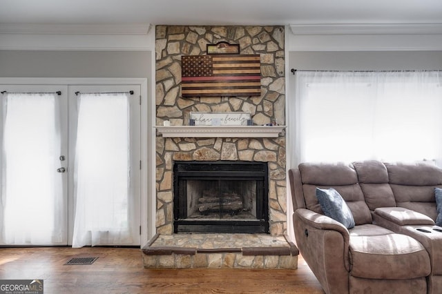 living area featuring crown molding, wood finished floors, visible vents, and a stone fireplace