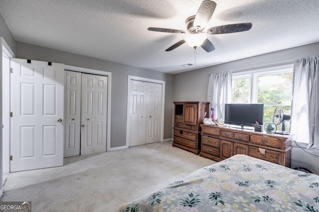 bedroom featuring visible vents, light carpet, a textured ceiling, ceiling fan, and multiple closets