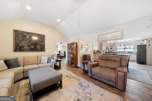 living room with a chandelier, light wood-style floors, and lofted ceiling