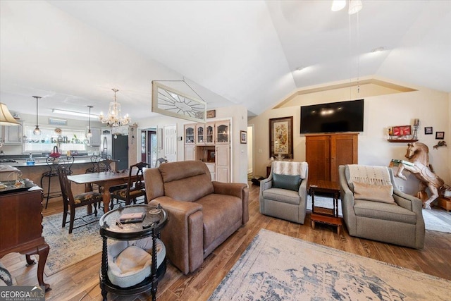 living area featuring light wood-style flooring, a notable chandelier, and vaulted ceiling