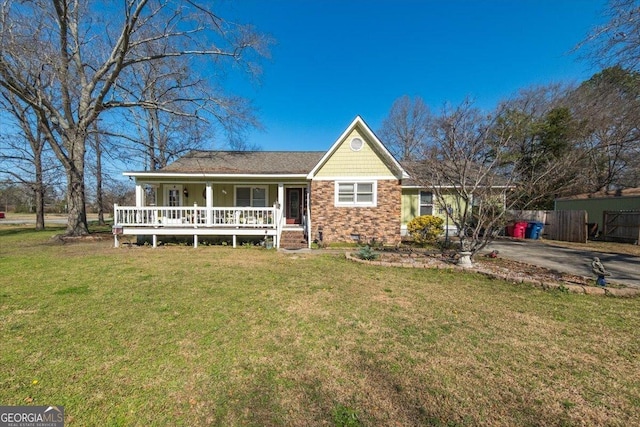 view of front of house featuring a front lawn, covered porch, stone siding, and driveway