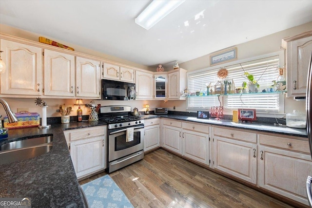 kitchen featuring a sink, stainless steel range with gas cooktop, black microwave, dark stone countertops, and wood finished floors