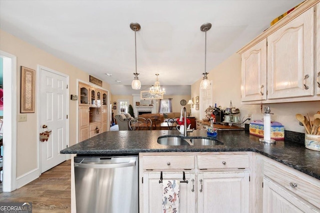 kitchen with dark countertops, stainless steel dishwasher, open floor plan, a sink, and pendant lighting