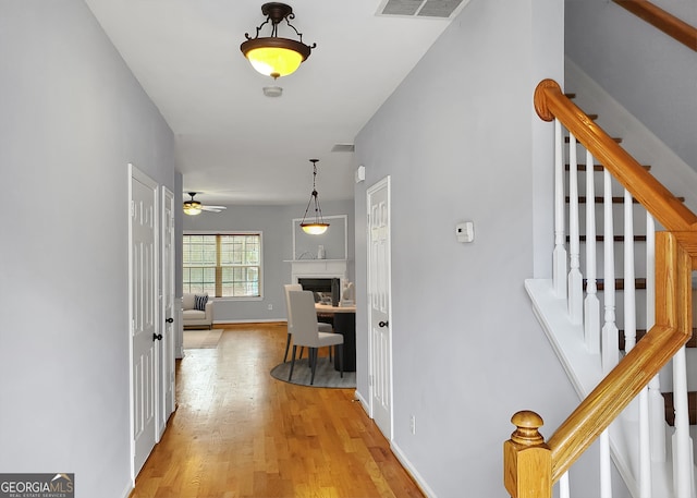 hallway with stairs, wood finished floors, visible vents, and baseboards